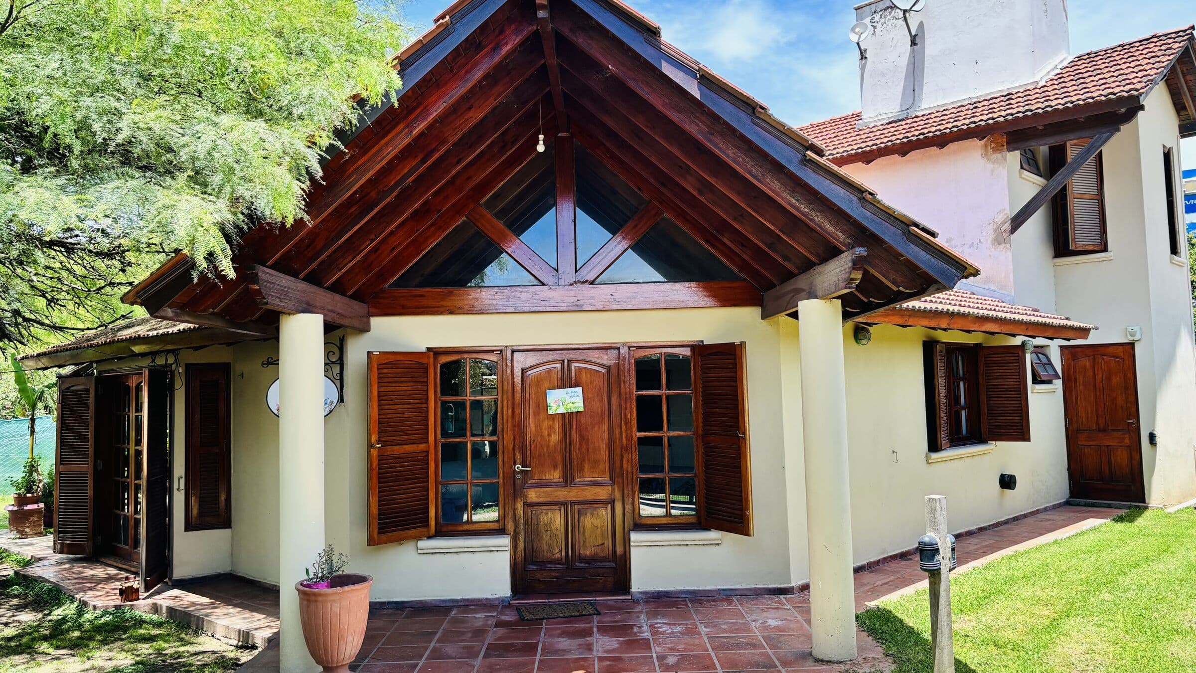 Frente de la casa con techo de madera a dos aguas, ventanales y galería